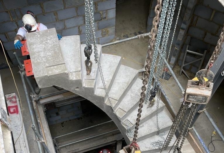 Curved concrete stair is installed with crane showing steel cleats for support