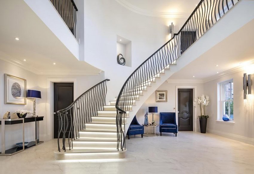 White grand staircase with black ballustrade in open hall with blue chairs close up