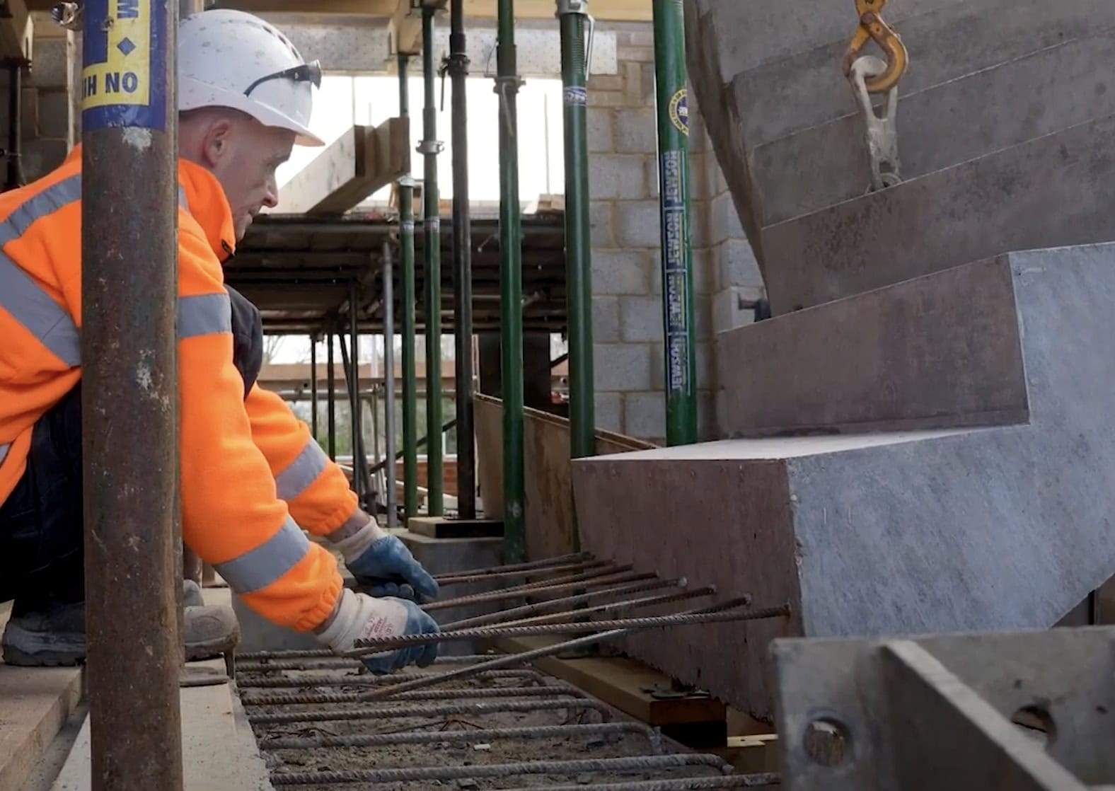 Construction worked guides curved staircase into position on building site with projecting reinforcement