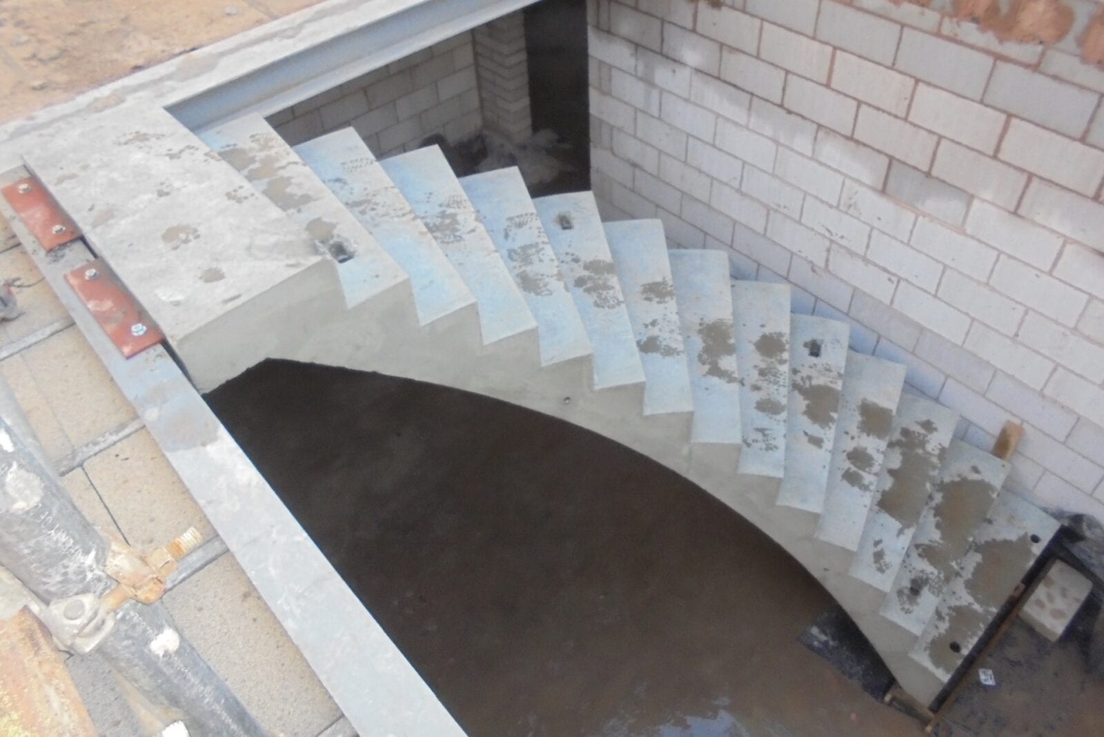 Installed concrete curved staircase with metal fixing cleets attached to concrete floor