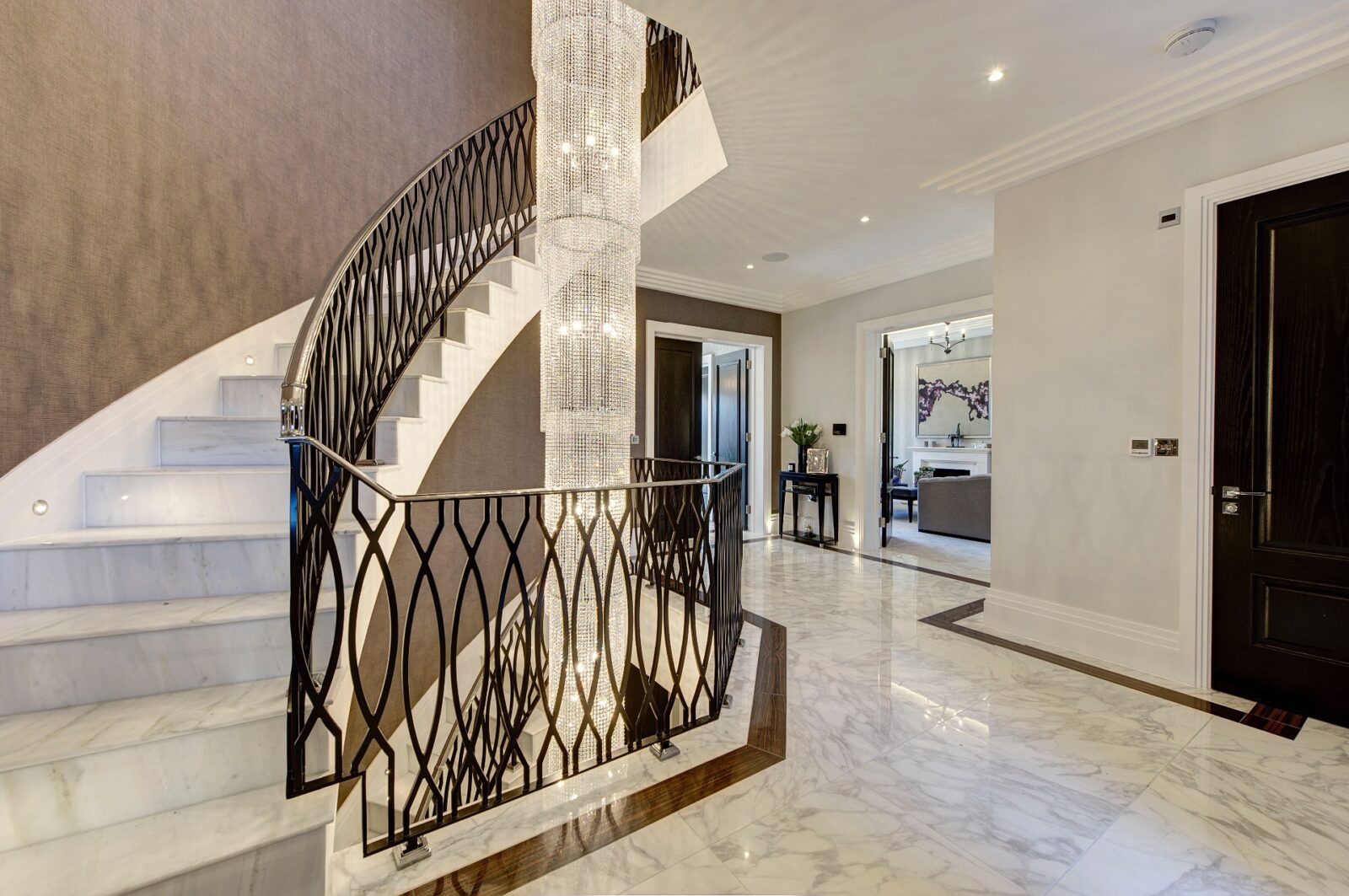 Large luxury chandelier hangs through void next to sweeping curved staircase in luxury home London Road Shenley