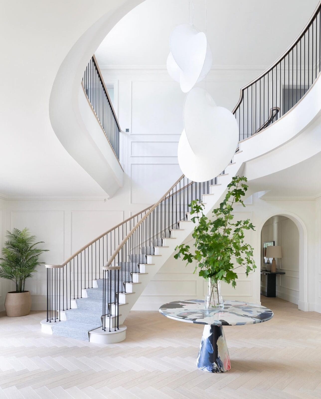 White luxury curved staircase with artistic chandelier and modern table with green plant